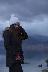 Portrait of smiling woman standing by lake against sky