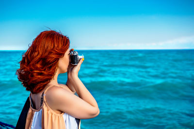 Rear view of woman photographing sea against sky