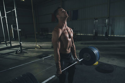 Shirtless male athlete lifting barbell in health club