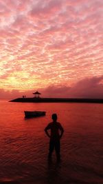 Silhouette man standing in sea against sky during sunset