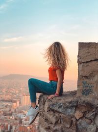 Woman looking at cityscape against sky during sunset