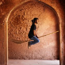 Side view of man levitating on broom against wall