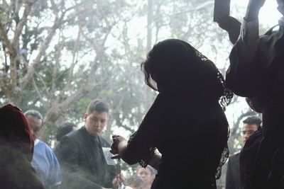 Rear view of people standing against trees