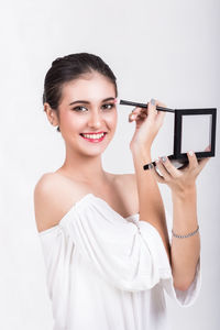 Portrait of smiling beautiful woman applying eyeshadow against white background