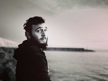 Portrait of young man standing at sea shore against sky