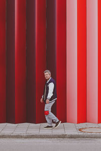 Side view of young man standing against red wall