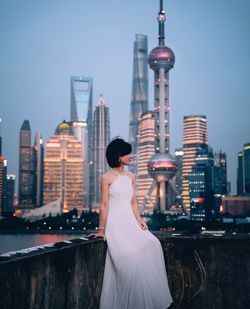 Woman standing by modern buildings against sky in city