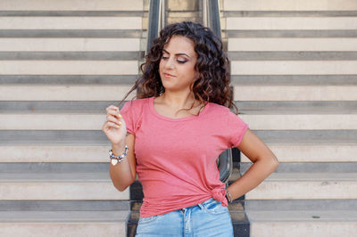Young women wearing t-shirt and jeans stays near the stairs and touch hairs