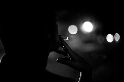 Close-up of silhouette woman smoking cigarette at night