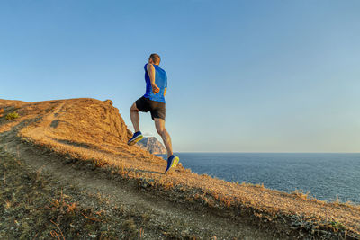 Back man runner athlete running uphill in background blue sky and sea