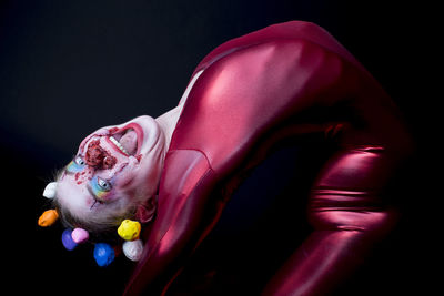 Portrait of woman with face paint wearing clown costume against black background