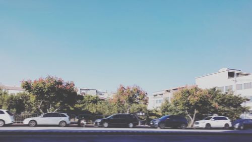 Cars on street by buildings against clear blue sky