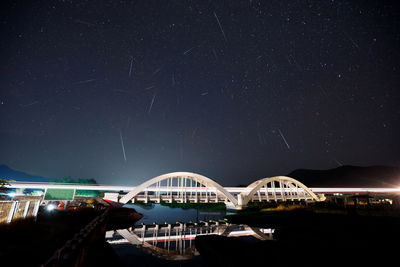 Illuminated bridge over river against sky at night
