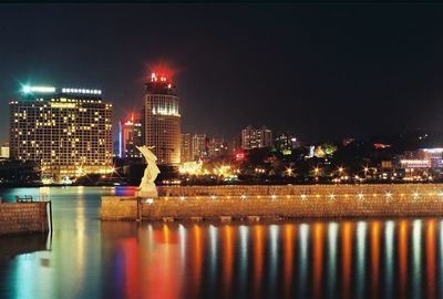 Illuminated buildings by river against sky at night