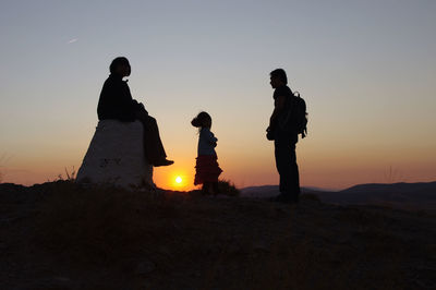 Rear view of silhouette people on field against sky during sunset