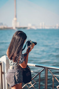 Rear view of woman photographing against sea