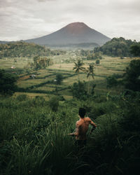 Rear view of shirtless man on field against sky