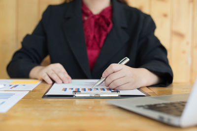 Midsection of businesswoman analyzing graphs on desk in office