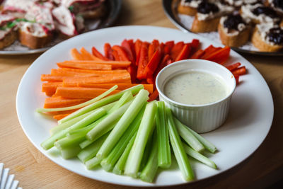 Vegetable sticks with dipping sauce on white plate, close up