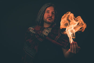 Young man wearing robe, holding fire against black background