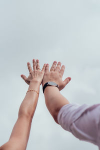 Low angle view of hand holding hands against sky