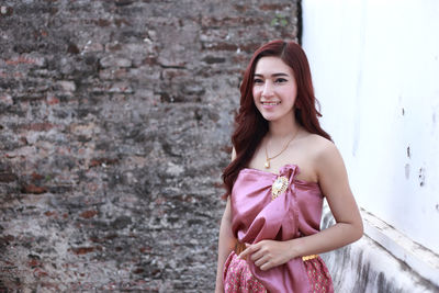 Portrait of smiling young woman standing against wall