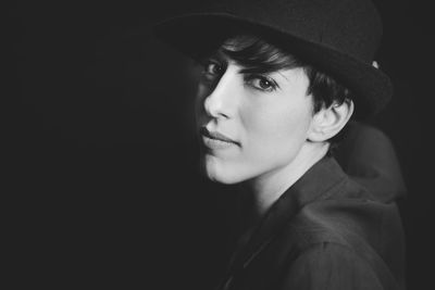 Portrait of young woman wearing hat against black background