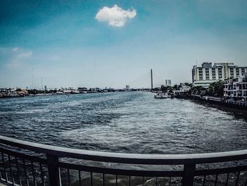 View of city at waterfront against cloudy sky