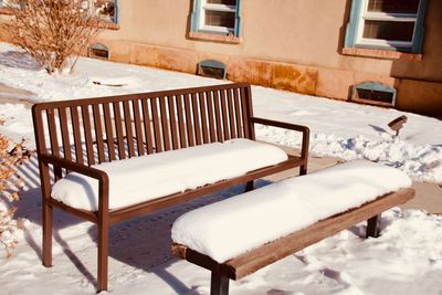 Empty chairs and tables in snow against building