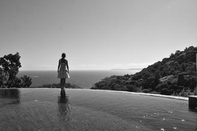Rear view of woman standing at poolside against sea and sky