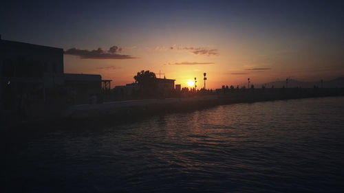 Silhouette city by sea against sky during sunset