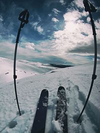 Skies with ski poles on snow covered mountain against cloudy sky