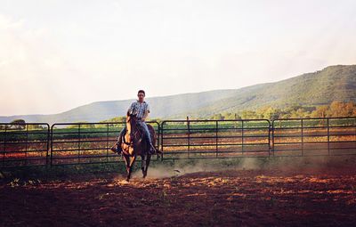 Young man riding on horse at ranch against clear sky