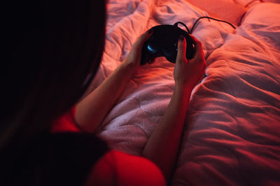 High angle view of young woman playing video game while relaxing on bed at home