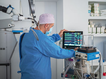 Professional doctor in medical uniform examining modern vital signs monitor during surgery in hospital