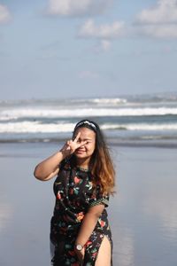 Woman gesturing peace sign while standing on shore at beach