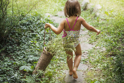 Rear view of girl carrying wooden basket with plants