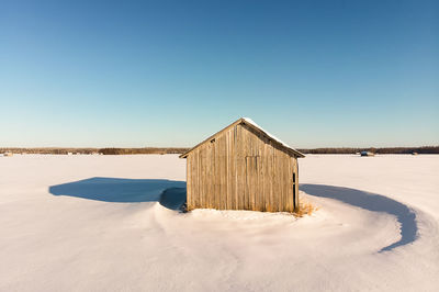 The winter sun creates strong shadows on the snowy fields. the barn house stands alone on the fields