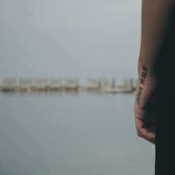 Cropped hand of woman with tattoo against lake