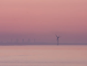Wind turbines on land against sky during sunset