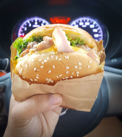 Cropped hand of person holding hamburger in car