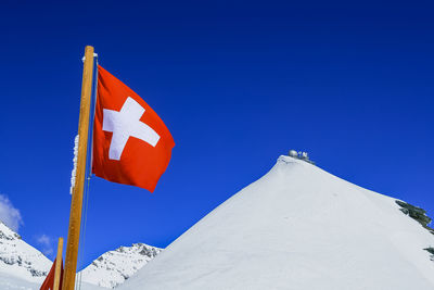 Swiss flag on snowcapped mountain against clear blue sky