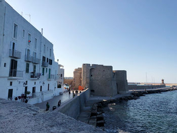 Buildings by sea against clear blue sky