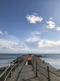 Pier at beach against blue sky