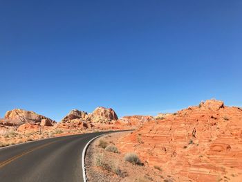 Road by rocky mountains against clear blue sky