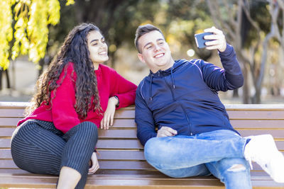 Friends taking selfie while sitting on park bench