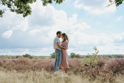 Side view of couple looking to each other and standing on field against sky