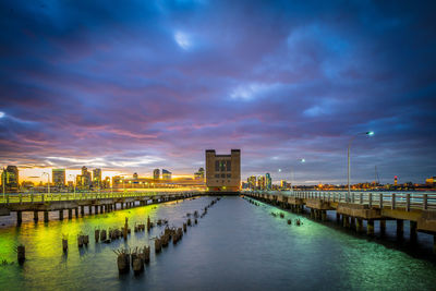 Illuminated bridge over river against cloudy sky in city