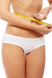 Midsection of woman measuring waist with tape measure against white background