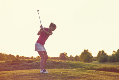 Full length of person on golf course on field against sky during sunset